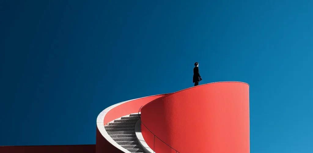 Illustration : une personne sur un promontoire qui se détache sur un ciel bleu profond, en haut d'un escalier rouge, pour illustrer l'expérience de l'agence Strategic Design créée par Agnès Broc