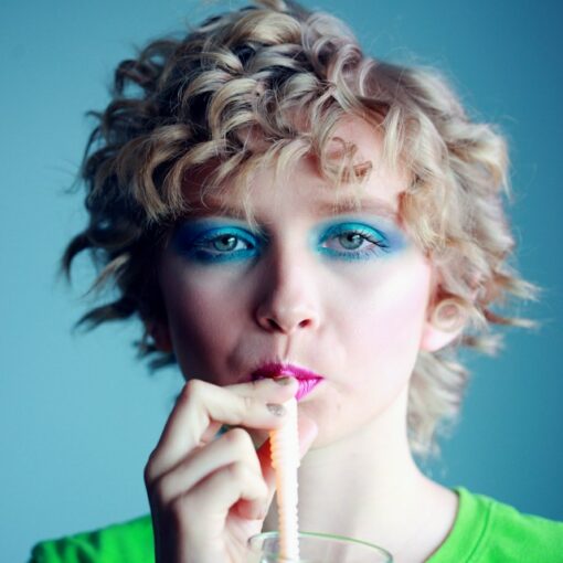 Photo d'une femme avec un tee shirt vert vif, des yeux maquillés en vert, du rouge à lèvres très rouge en train de boire avec une paille, pour illustrer cet article sur l'importance de connaître ses cibles de communication pour communiquer efficacement