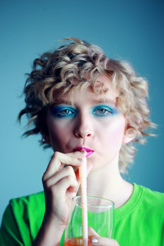 Photo d'une femme avec un tee shirt vert vif, des yeux maquillés en vert, du rouge à lèvres très rouge en train de boire avec une paille, pour illustrer cet article sur l'importance de connaître ses cibles de communication pour communiquer efficacement