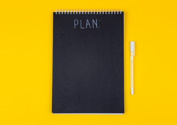 Un cahier et un stylo sur fond jaune vif pour illustrer cet article sur les 10 étapes à suivre pour réussir ses événements d'entreprise