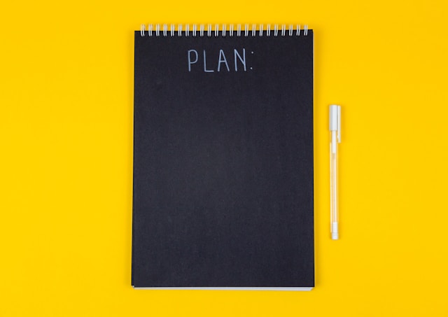 Un cahier et un stylo sur fond jaune vif pour illustrer cet article sur les 10 étapes à suivre pour réussir ses événements d'entreprise